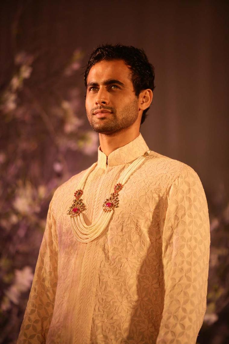 A model sporting a nehru jacket with a multi-string pearl necklace featuring kundan polki and gem-set brooches by Anmol Jewellers.