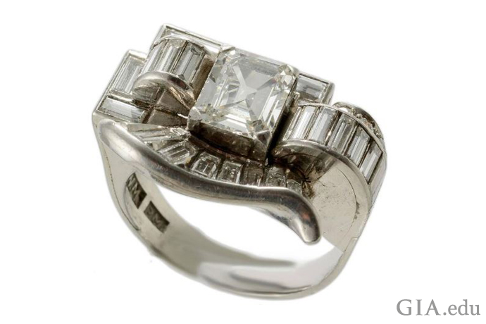 Diamond baguettes form curved lines in this vintage Retro-era engagement ring. A 1.50 ct emerald cut diamond is the center stone. 